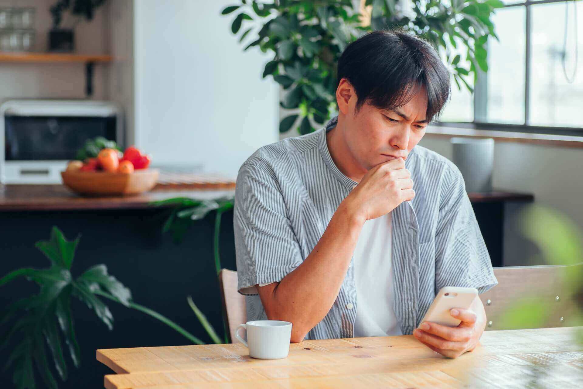 悩んだ表情でスマートフォンを見る男性